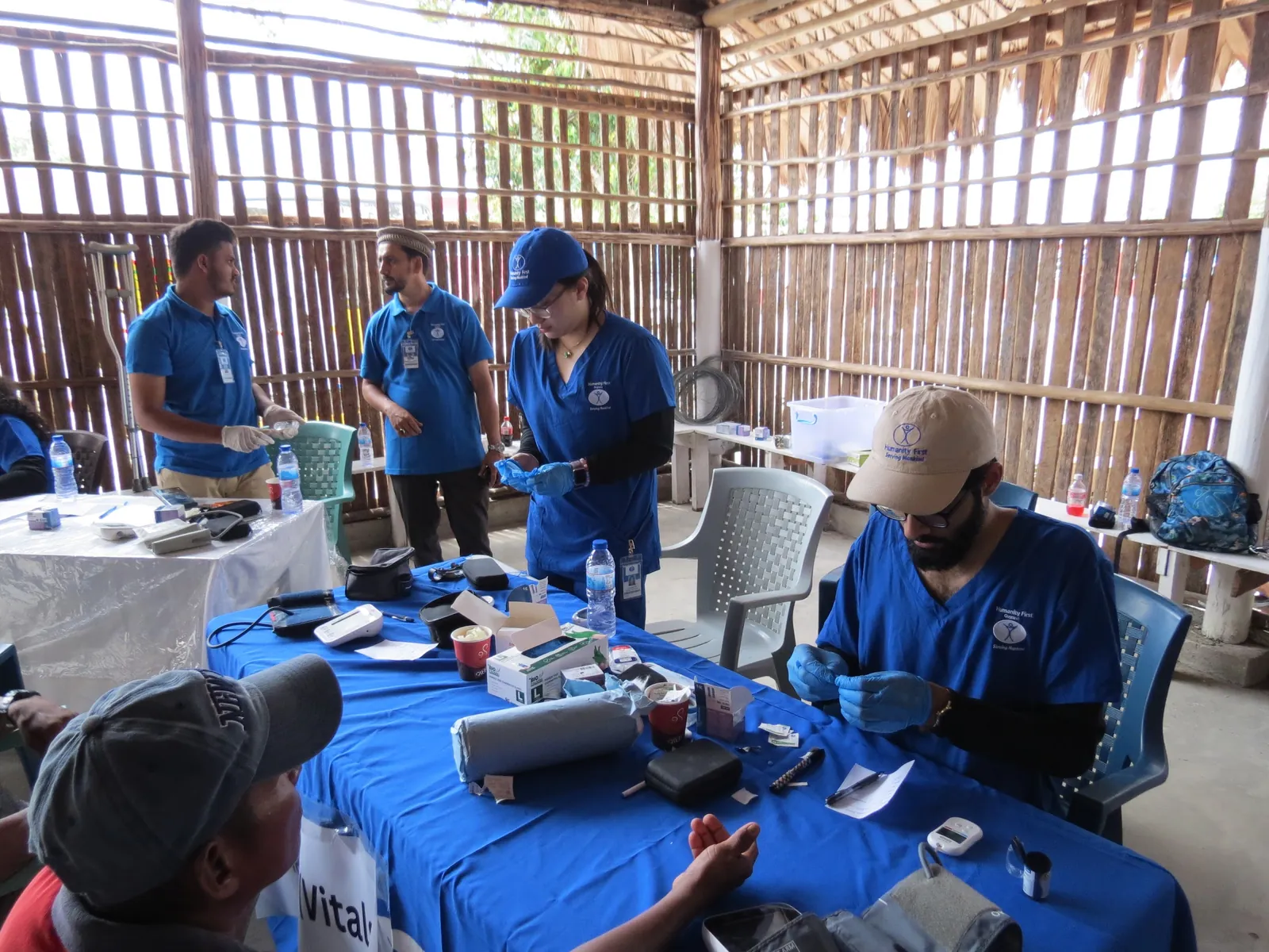 Students in blue scrubs and gloves prepare glucose meters and supplies at the vitals table of a medical camp in Guyana