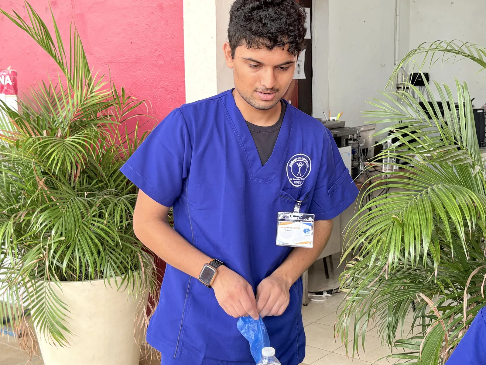 A student volunteer in blue scrubs pulls on gloves while preparing for patients on the December 2025 Mexico mission