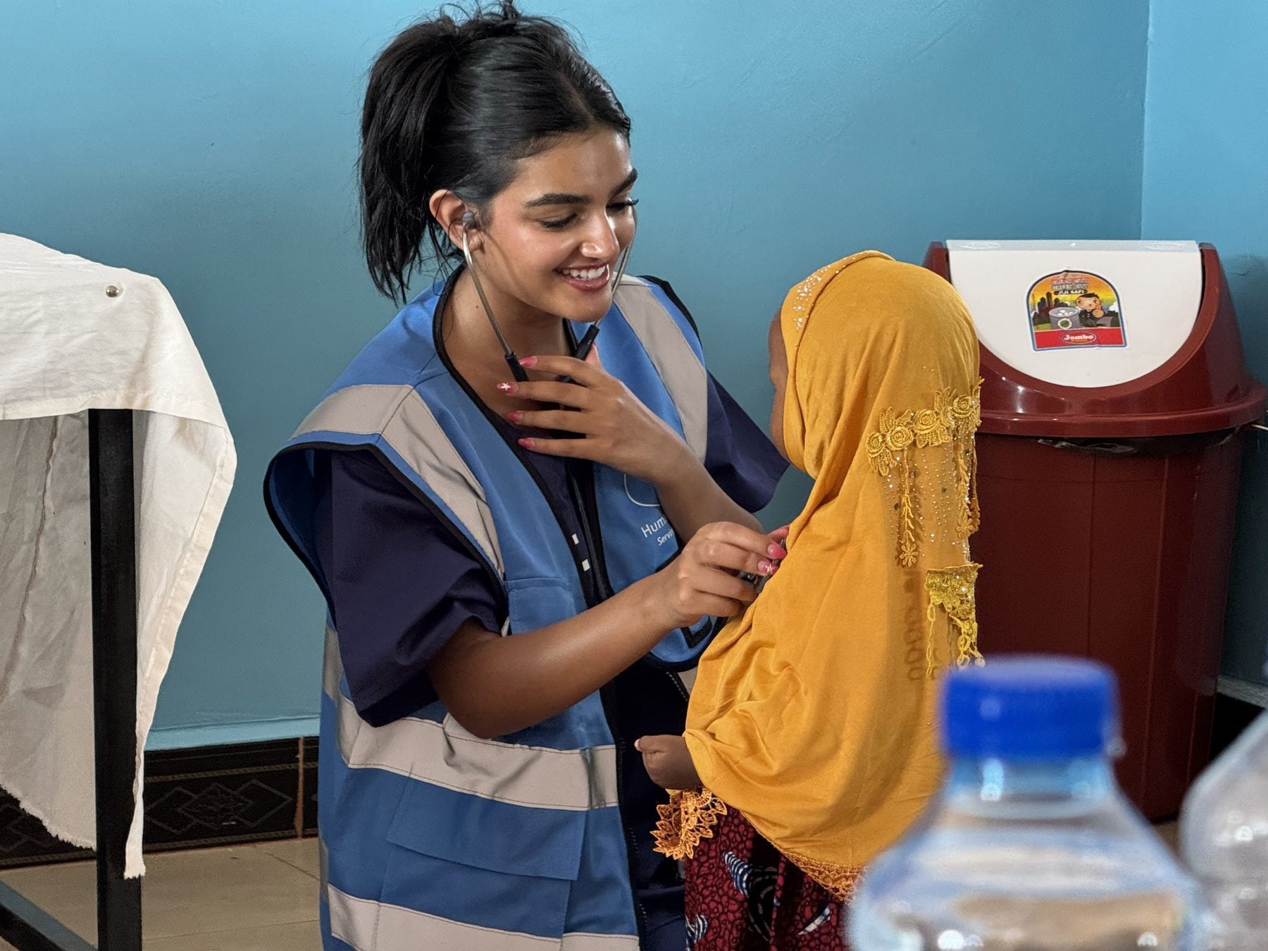 A student volunteer in a Humanity First vest helps a young patient in a headscarf in Tanzania