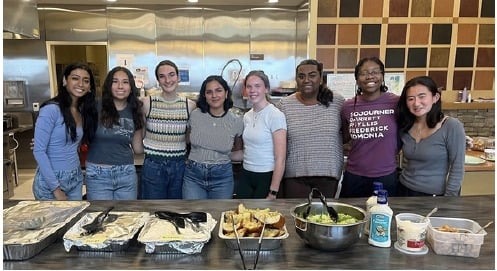 Eight chapter volunteers stand behind trays of food they prepared at a community kitchen