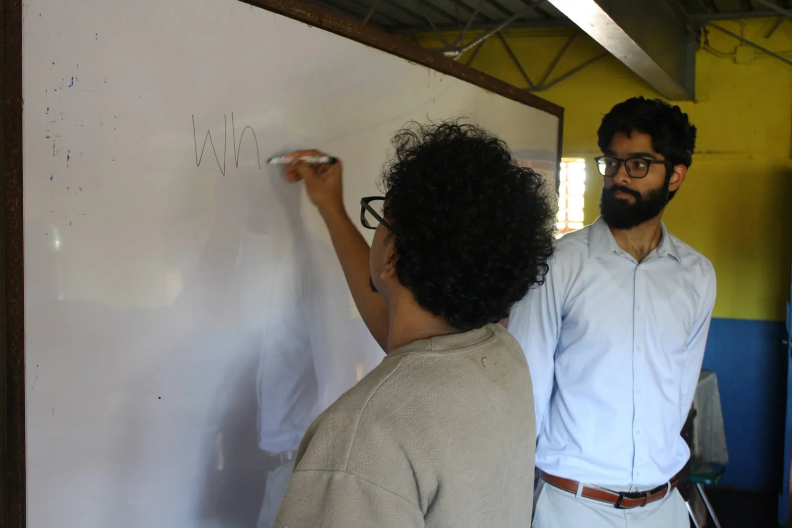 A volunteer writes on the whiteboard at the front of a classroom at Epping Forest Primary School