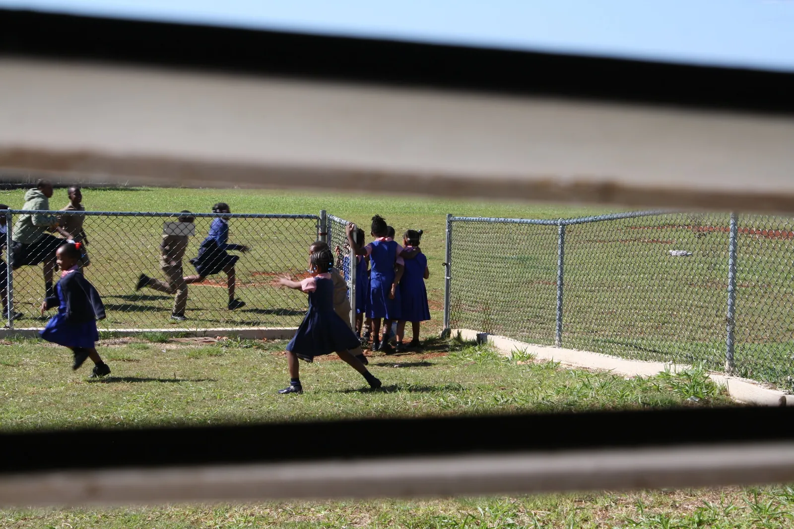 Students in school uniforms play on the grassy schoolyard at recess during The Education Project week in Jamaica