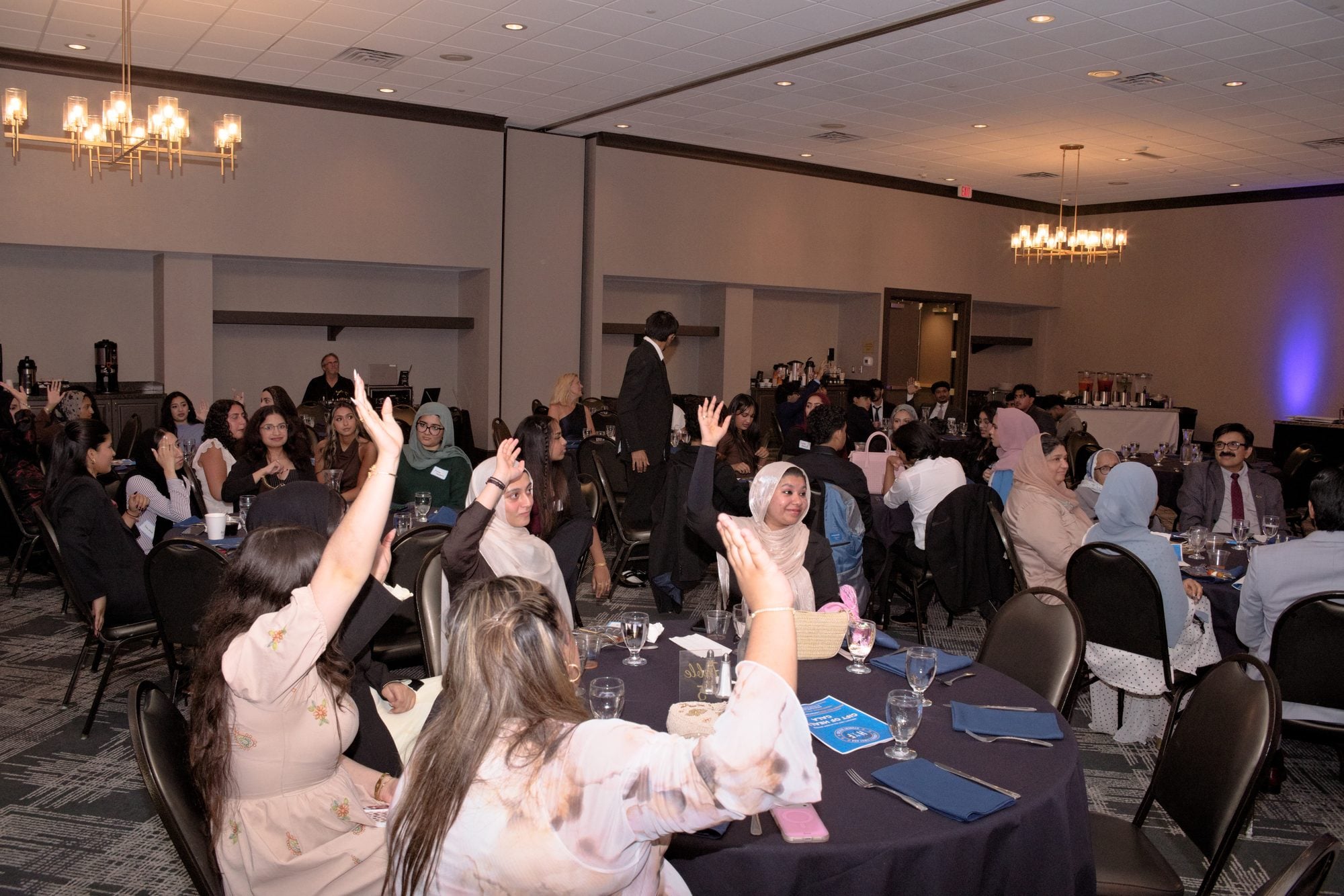 Guests across the Gift of Health Gala ballroom raise their hands during the pledge drive