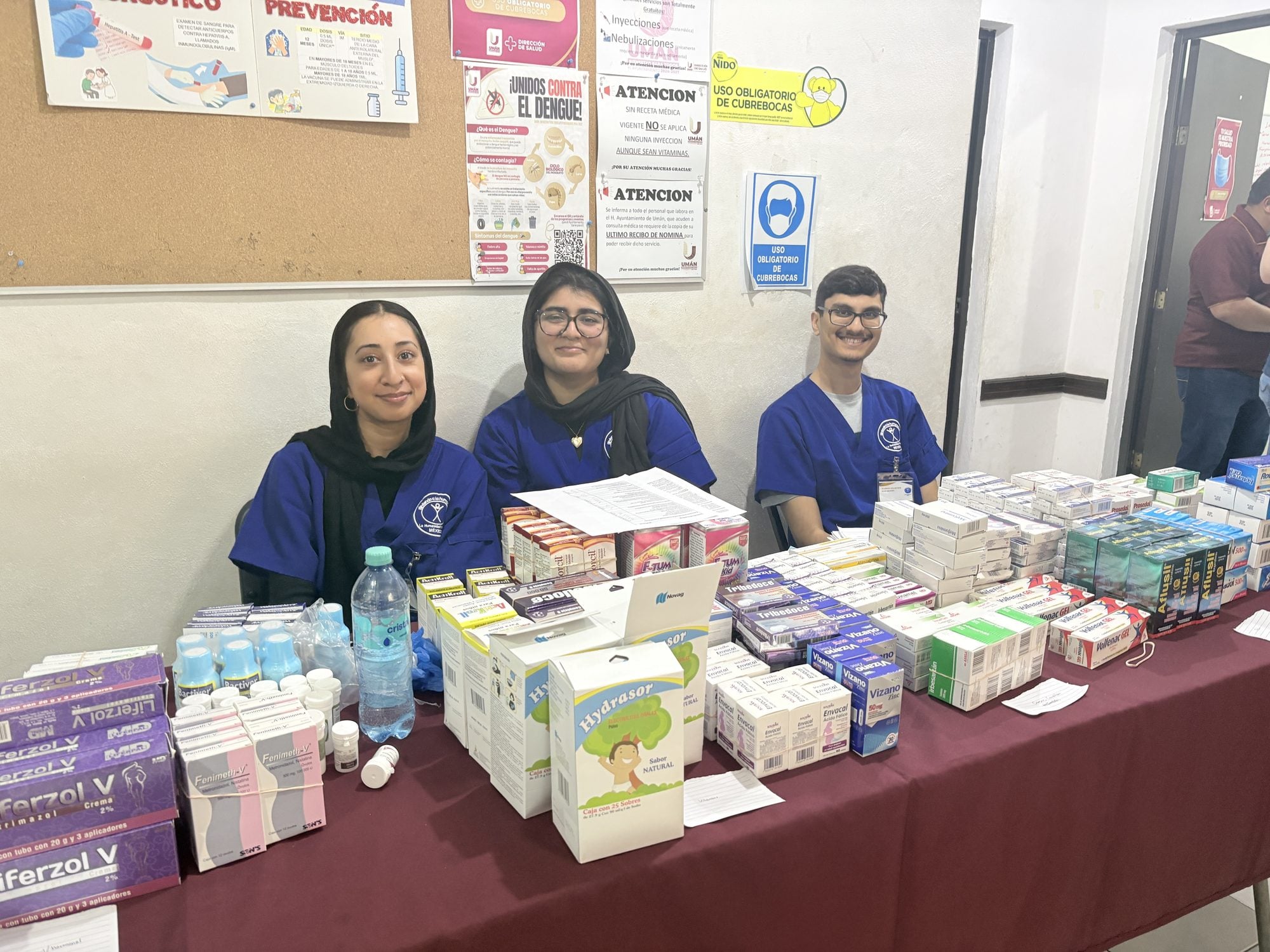 Three student volunteers in scrubs staff the mission pharmacy table stocked with medications in Mexico