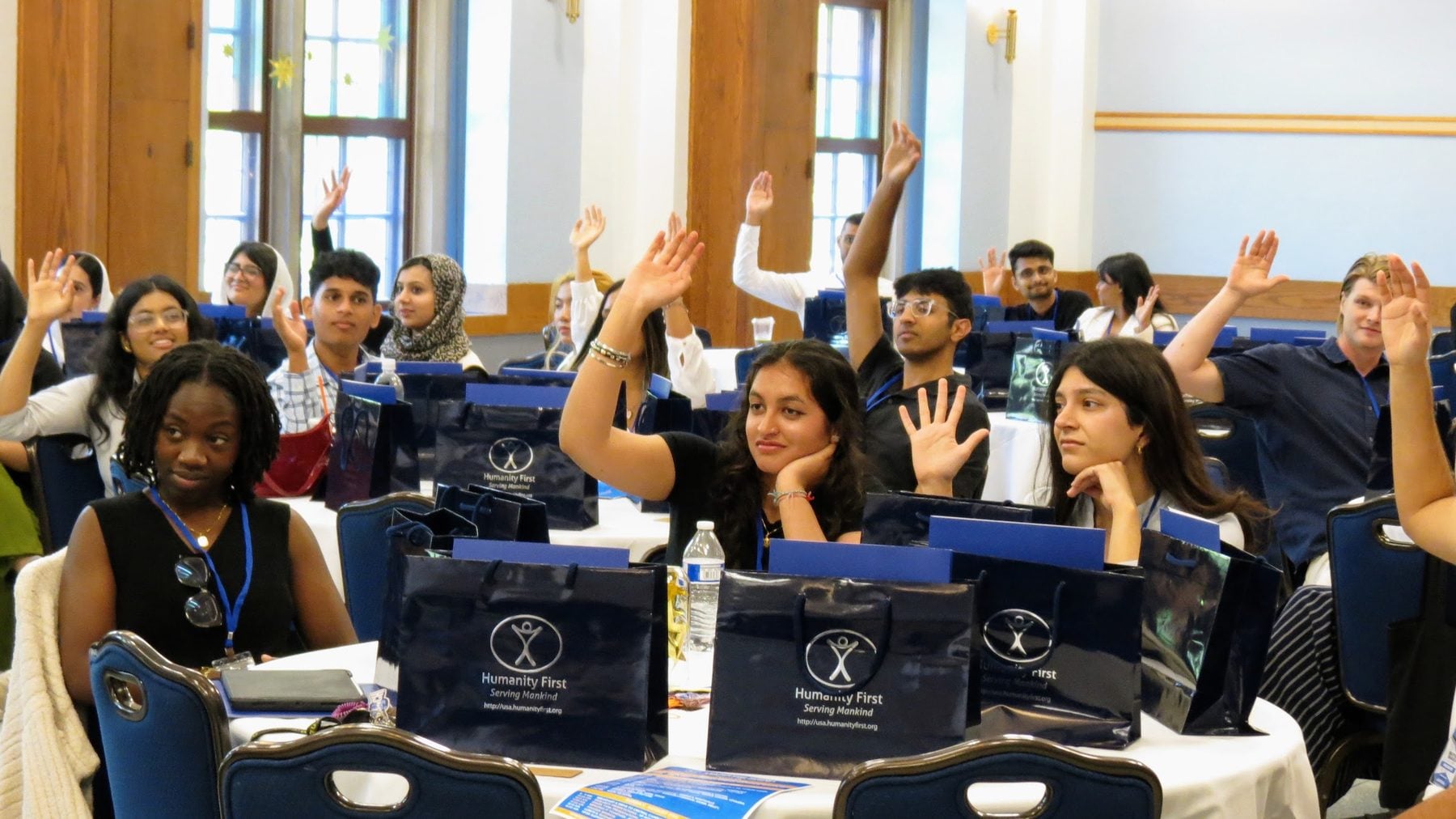 A room full of Summit 2024 delegates raise their hands at the University of Michigan