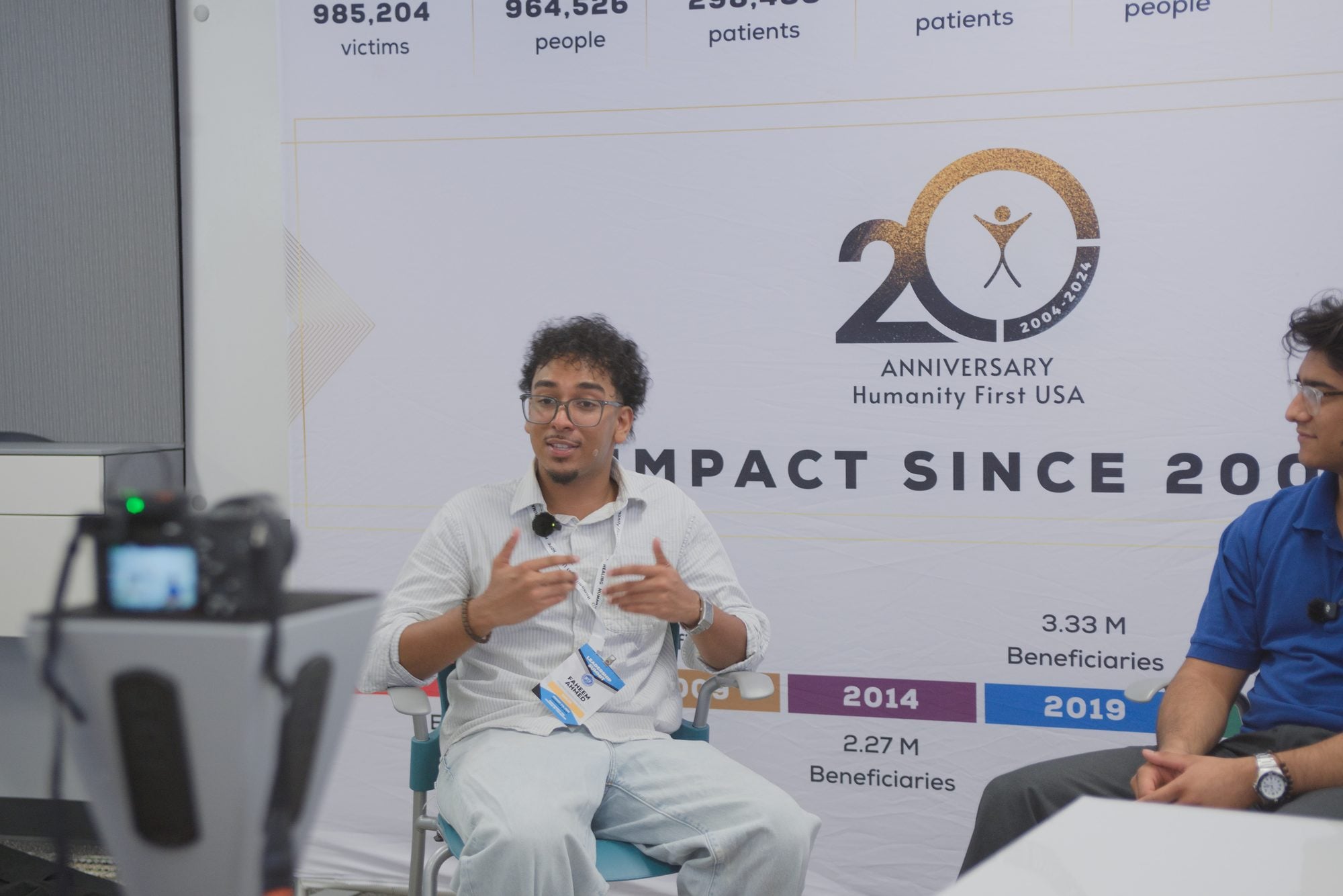 A delegate speaks beside the Humanity First USA 20th anniversary backdrop at Summit 2026