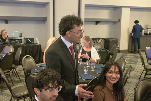 A student in a suit greets guests at a banquet table, drawing smiles at the Gift of Health Gala 2026.
