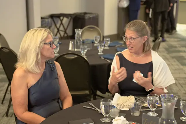 Two women in evening wear share an animated conversation at a banquet table at the Gift of Health Gala 2026.
