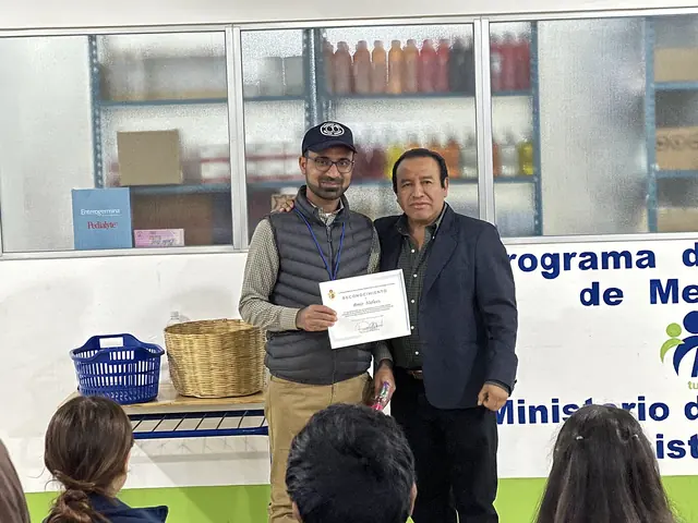 A mission leader and a local official hold up a certificate together in front of a Ministry of Health program banner in Guatemala.