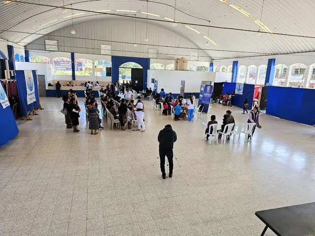 A wide view of a large municipal hall set up as a Gift of Health clinic, with patients seated in waiting areas across the floor.