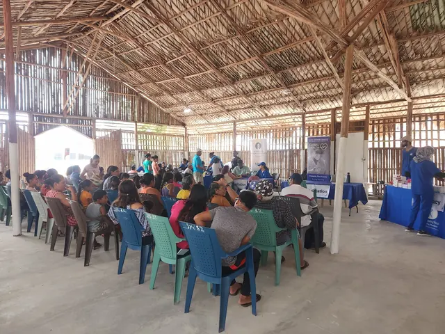 Rows of patients sit in plastic chairs under a large thatched roof pavilion as volunteers staff tables at the Gift of Health Guyana clinic.
