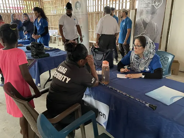 A physician in a headscarf and blue scrubs speaks with a patient across a consultation table at the Gift of Health Guyana clinic.