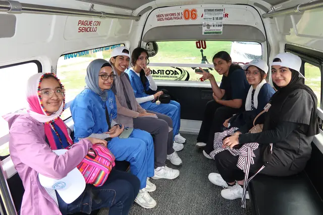 Smiling students, several in blue scrubs and white caps, ride together in the back of a minibus on the way to the clinic in Mexico.