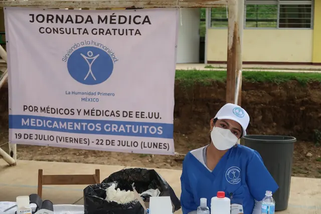 A masked student volunteer beside the jornada médica sign advertising free consultations
