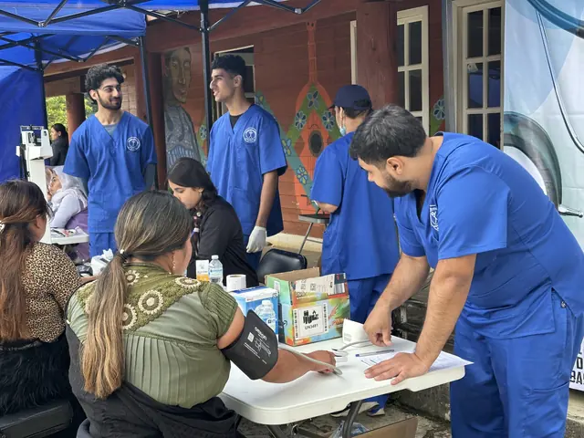 Student volunteers in blue scrubs take a patient's blood pressure at the intake table