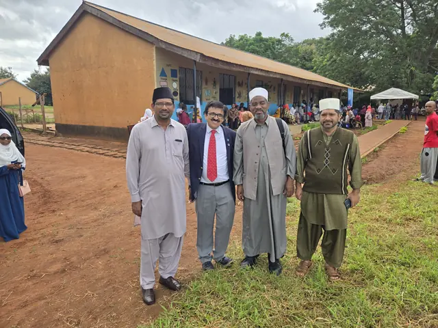 Four mission leaders in traditional dress and suits stand together on the grass in front of the clinic building in Tanzania.