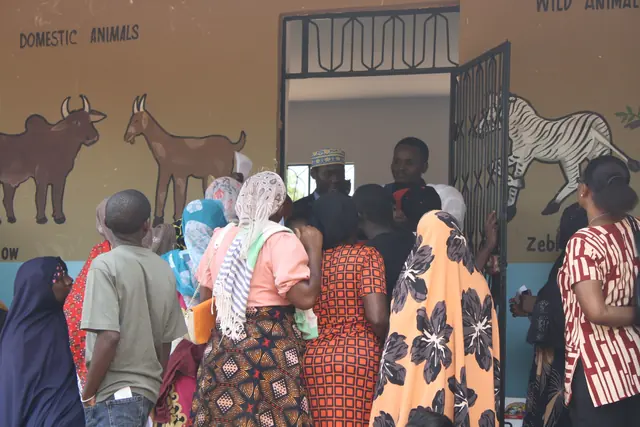 Patients crowd the doorway of a classroom painted with farm animal murals as they wait to enter the clinic in Tanzania.