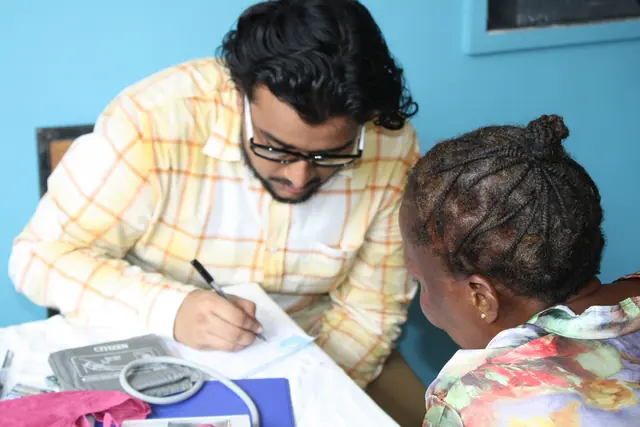 A student volunteer writes notes while consulting with a patient