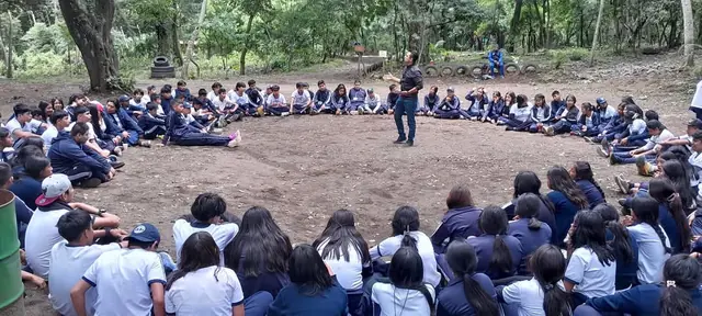 Students sit in a large circle outdoors while a leader speaks from the center at the Masroor Ahmad School in Guatemala.