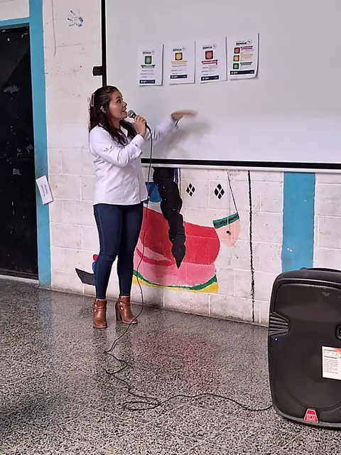 A teacher speaks into a microphone and points to the board during a school presentation at the Masroor Ahmad School in Guatemala.