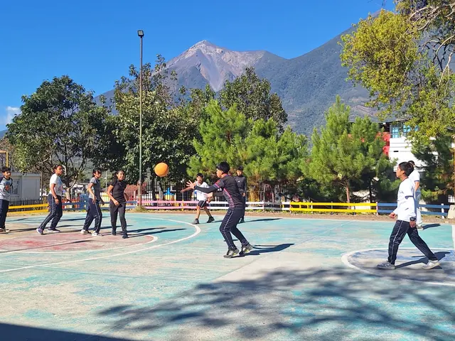 Students play basketball on the court under a clear sky with a volcano beyond the trees at the Masroor Ahmad School in Guatemala.
