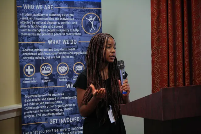 A student speaker gestures while addressing delegates with a microphone during a session at the HFSD Leadership Summit '23.
