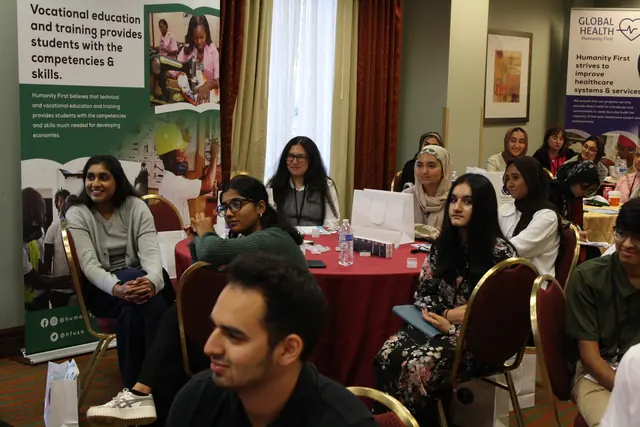 Attentive delegates seated at tables follow a presentation in front of Humanity First program banners at the HFSD Leadership Summit '23.