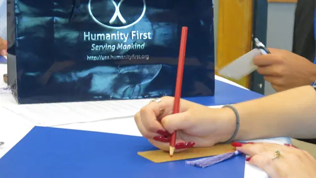 A hand fills in a Humanity First pledge card with a red pencil