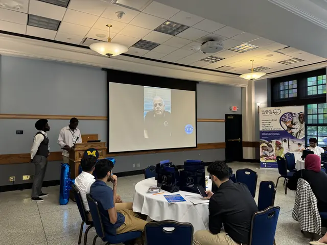 Delegates at round tables watch a speaker join by video on a large screen at the 2024 HFSD Leadership Summit.