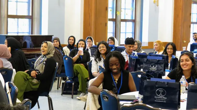 Smiling delegates seated at tables with summit bags enjoy a session at the 2024 HFSD Leadership Summit.