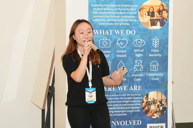 A student speaks into a microphone in front of a Humanity First Student Division banner at the HFSD Leadership Summit 2026.