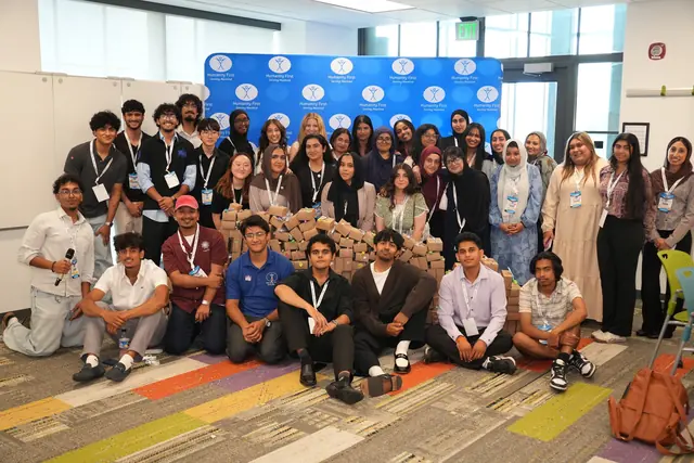 A large group of participants poses behind a wall of finished kit boxes before a Humanity First backdrop at the HFSD Leadership Summit 2026.